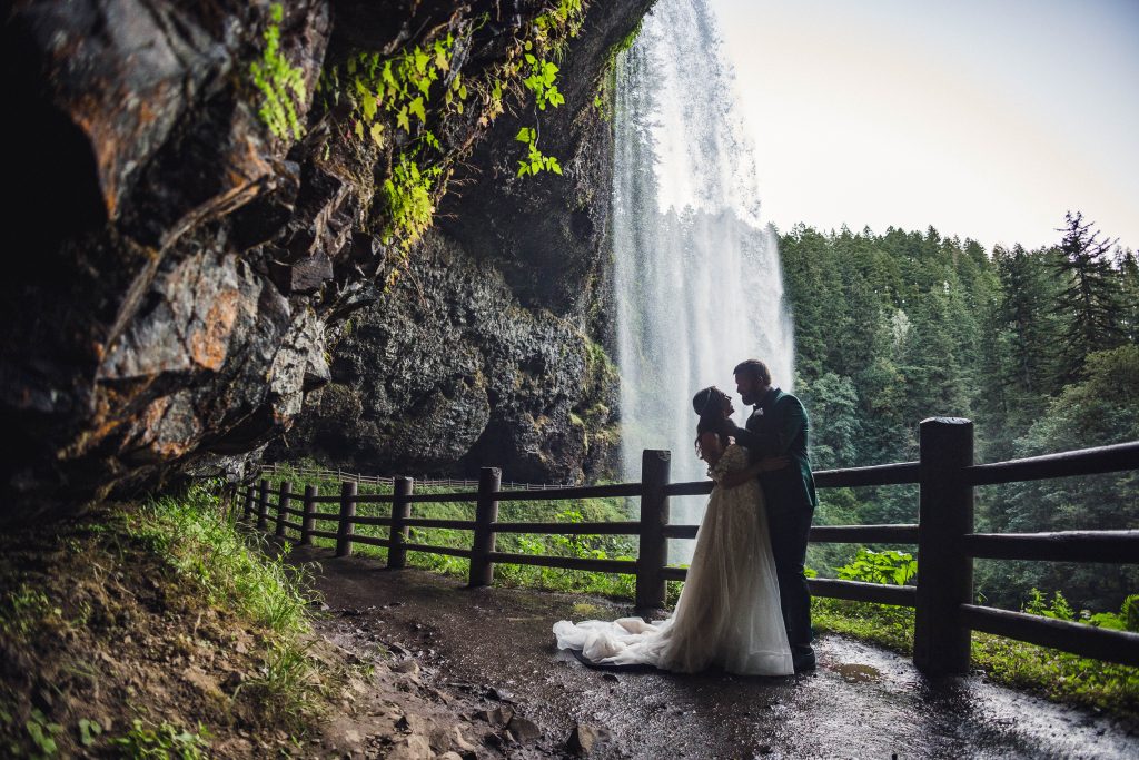 Bride and Groom stand under the South Falls at Silver Falls State Park Wedding Photographs