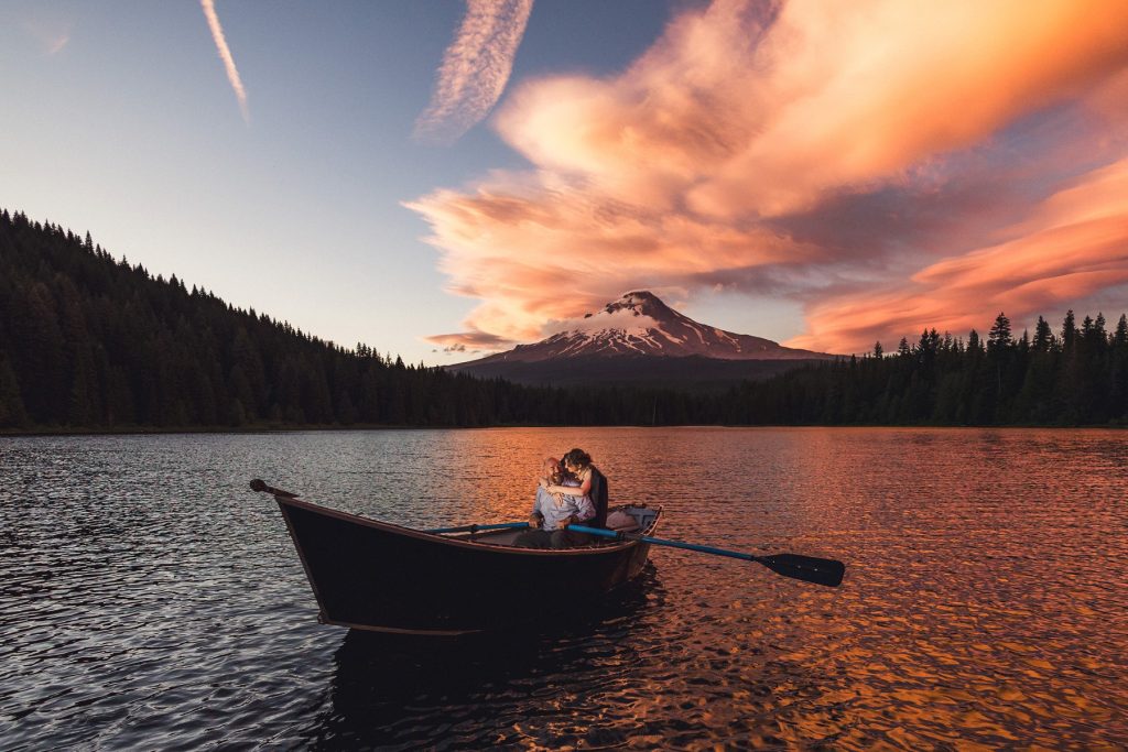 Epic Trillium Lake Engagement Photos, a couple on a row boat in the lake with the mountain and sunset and pink clouds behind them